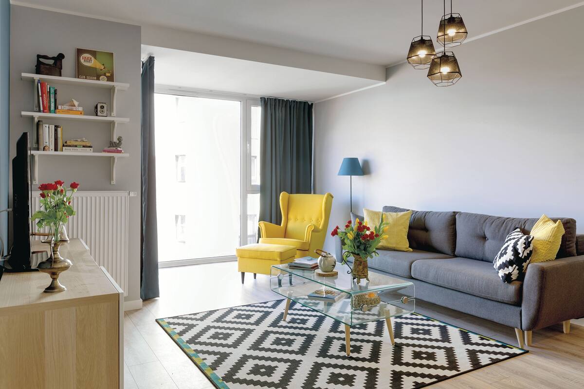 A modern living room with a glass coffee table, a sofa, a yellow armchair, and a bookshelf.