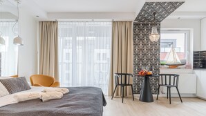 A modern hotel room with a large bed, a dining area with a table and chairs, and a view of the city through large windows. - Hopfen by Little Heaven (Gdansk)