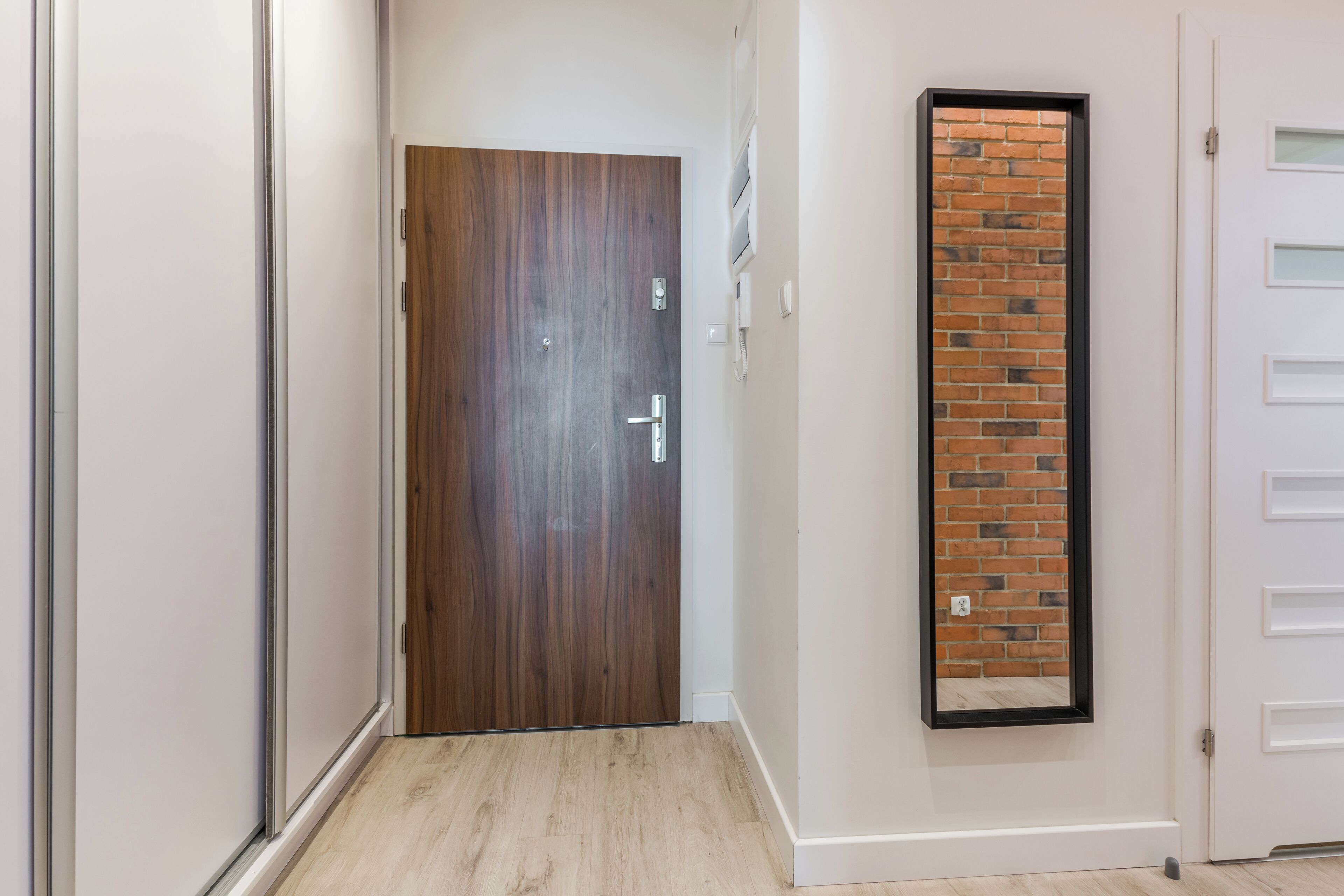 A hallway with a wooden door, a brick accent wall, and a white door with a black frame.