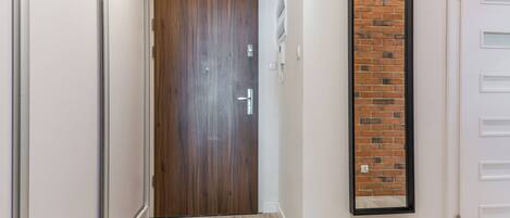 A hallway with a wooden door, a brick accent wall, and a white door with a black frame.