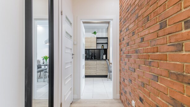 A narrow hallway with a brick wall on one side and a white door on the other. - Hopfen by Little Heaven (Gdansk)