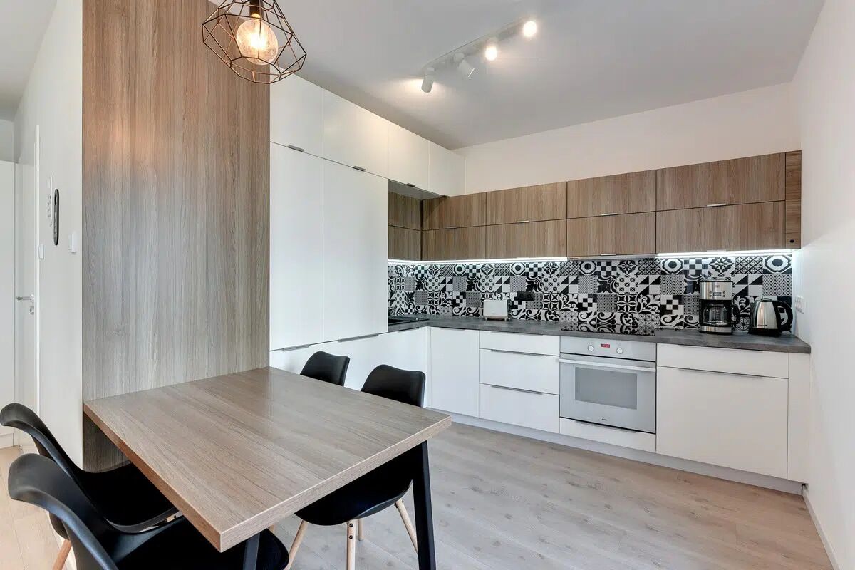 A modern kitchen with a wooden table and chairs, a patterned backsplash, and built-in cabinets.