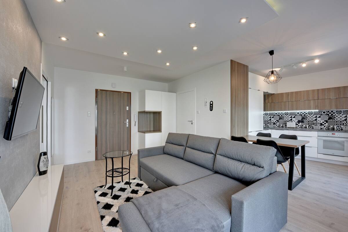 A modern living room with a grey sectional sofa, a small round table, and a black-and-white rug.