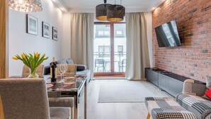 A modern living room with a dining area, a TV mounted on a brick wall, and a view through a glass door. - Hopfen by Little Heaven (Gdansk)