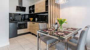 A modern kitchen with a dining area, featuring a glass-top table, grey upholstered chairs, and a decorative hanging light fixture. - Hopfen by Little Heaven (Gdansk)