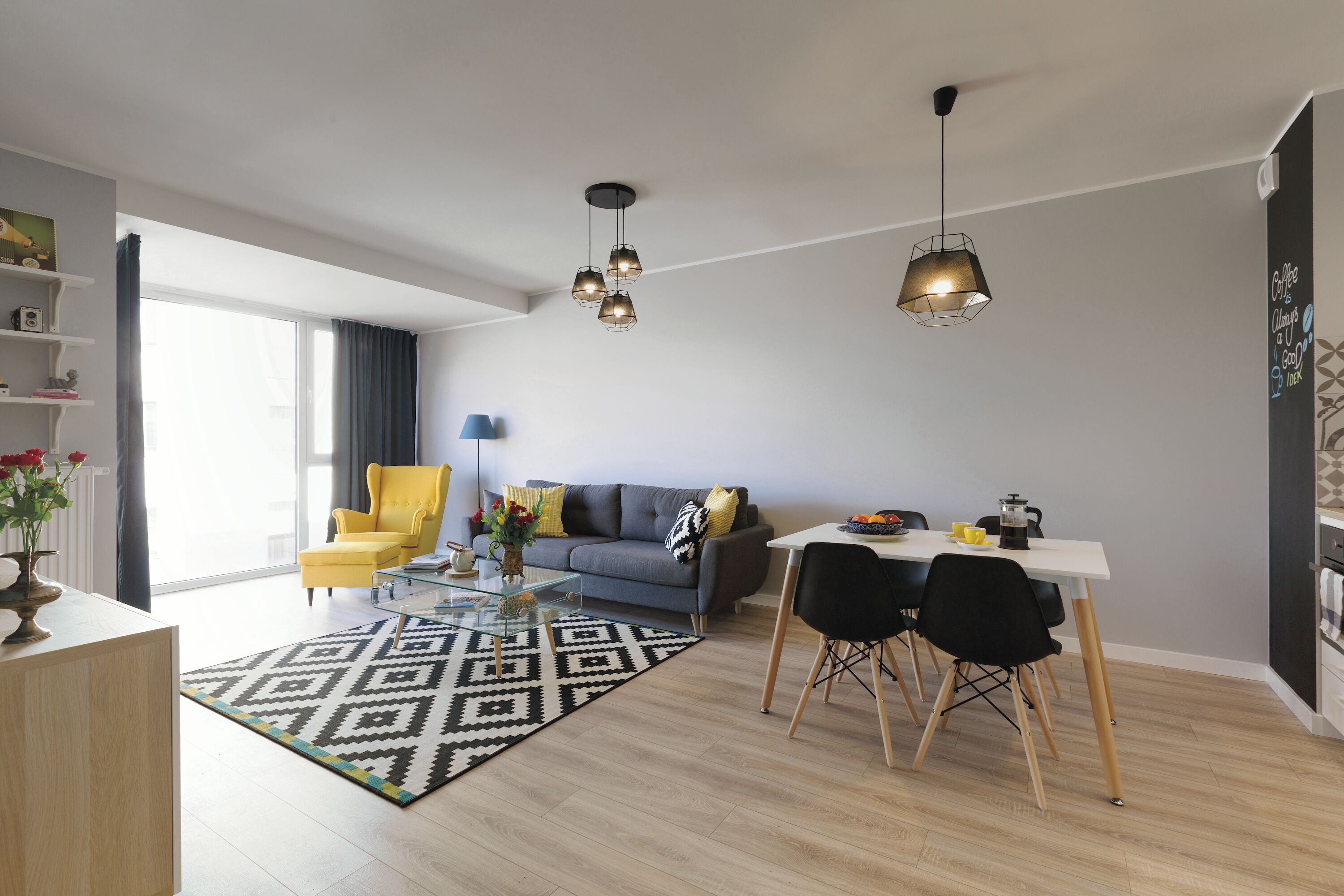 Een moderne woonkamer met een bank, een gele fauteuil, een eettafel en een koffiehoek.