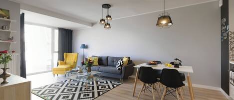 Een moderne woonkamer met een bank, een gele fauteuil, een eettafel en een koffiehoek.