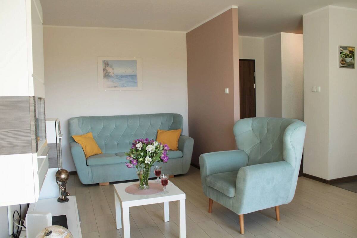 A living room with a light blue sofa, a matching armchair, a small white coffee table with a vase of flowers, and a painting on the wall.