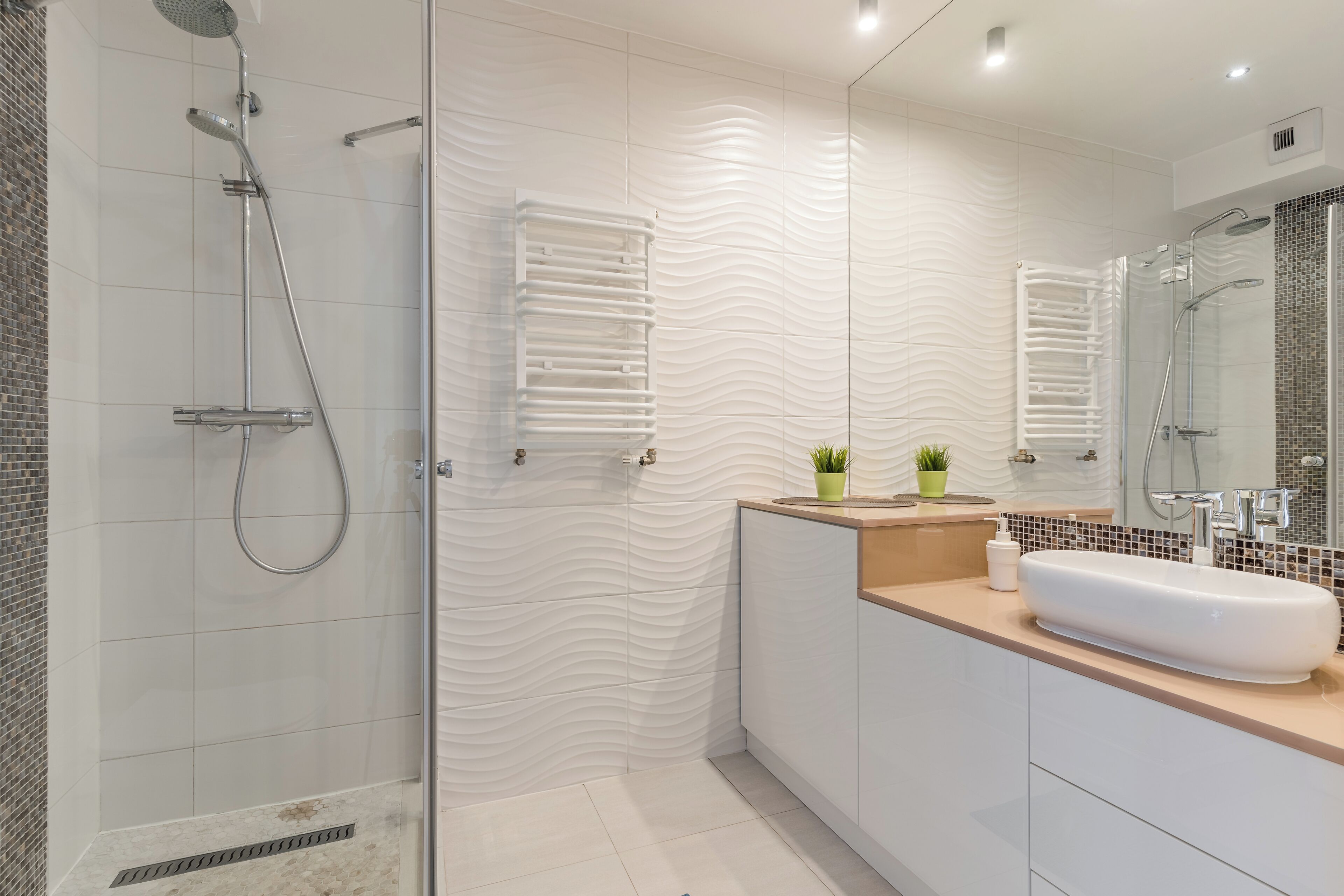A modern bathroom with a glass-enclosed shower, a white sink, and a mirror with a textured backsplash.