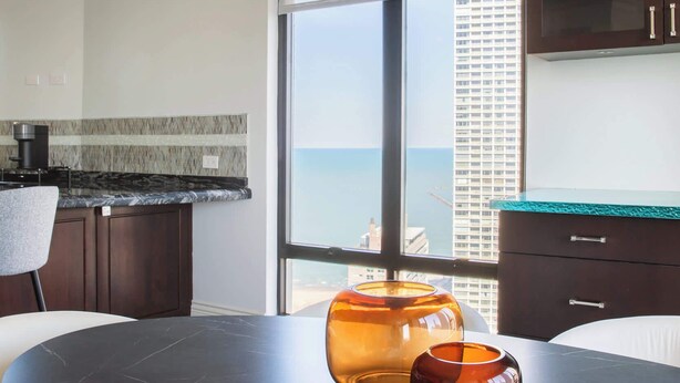A modern kitchen with a dark marble countertop, a round dining table, and a view of the city through large windows. - Luxury Designer Penthouse 3803 | Pool | Gold Coast (Chicago)