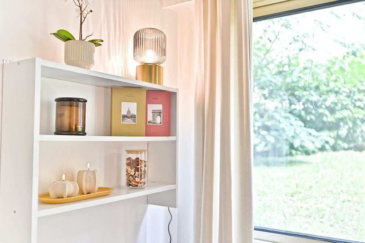 A bookshelf with decorative items, a candle, and a glass container with wood shavings.