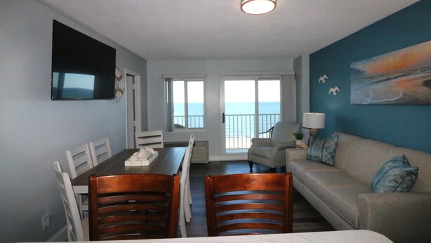 A room with a dining table, chairs, a sofa, a TV, and a painting.