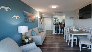 A modern living room with a sofa, a dining table with chairs, and a kitchen in the background.