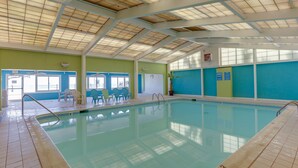 An indoor swimming pool with a tiled floor, clear water, and a ceiling with skylights.