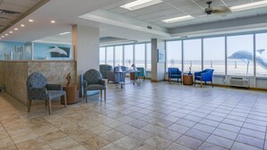 A spacious lobby with a high ceiling, large windows, and a view of the beach.