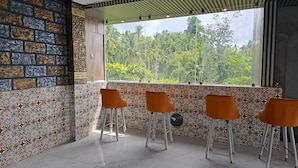 A room with a patterned wall, a window with a view of greenery, and four orange chairs. - HOTEL KANGAROO (Ferrurgunj)