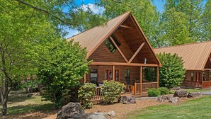 A log cabin with a porch, surrounded by trees and rocks.