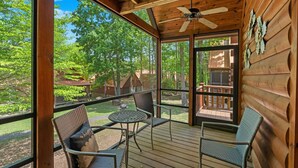 A wooden deck with two chairs and a small table, overlooking a forested area.