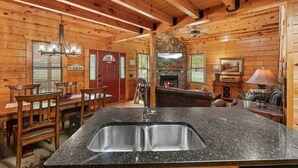 A cabin interior with a stone fireplace, wooden dining area, granite countertop with a sink, and a cozy seating area.