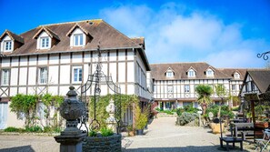 Un patio europeo tradicional con edificios de entramado de madera, una fuente de piedra y mobiliario exterior.