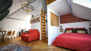 A loft-style bedroom with a red sofa, a bed with red bedding, a wooden ladder, and a chandelier. - Close to beach and amenities (Dives-sur-Mer)
