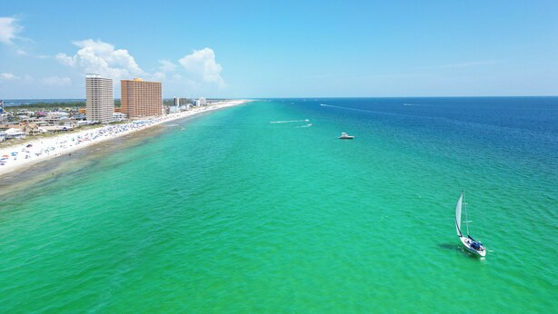 Un paisaje urbano costero con una playa, aguas turquesas cristalinas y un velero.