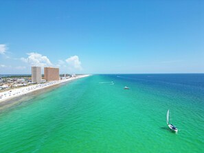 Eine Küstenlandschaft mit Strand, klarem türkisblauem Wasser und einem Segelboot.