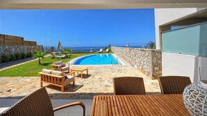 A poolside area with a view of the ocean, stone walls, and outdoor furniture. - Villa Kazoulis (Kalathas)