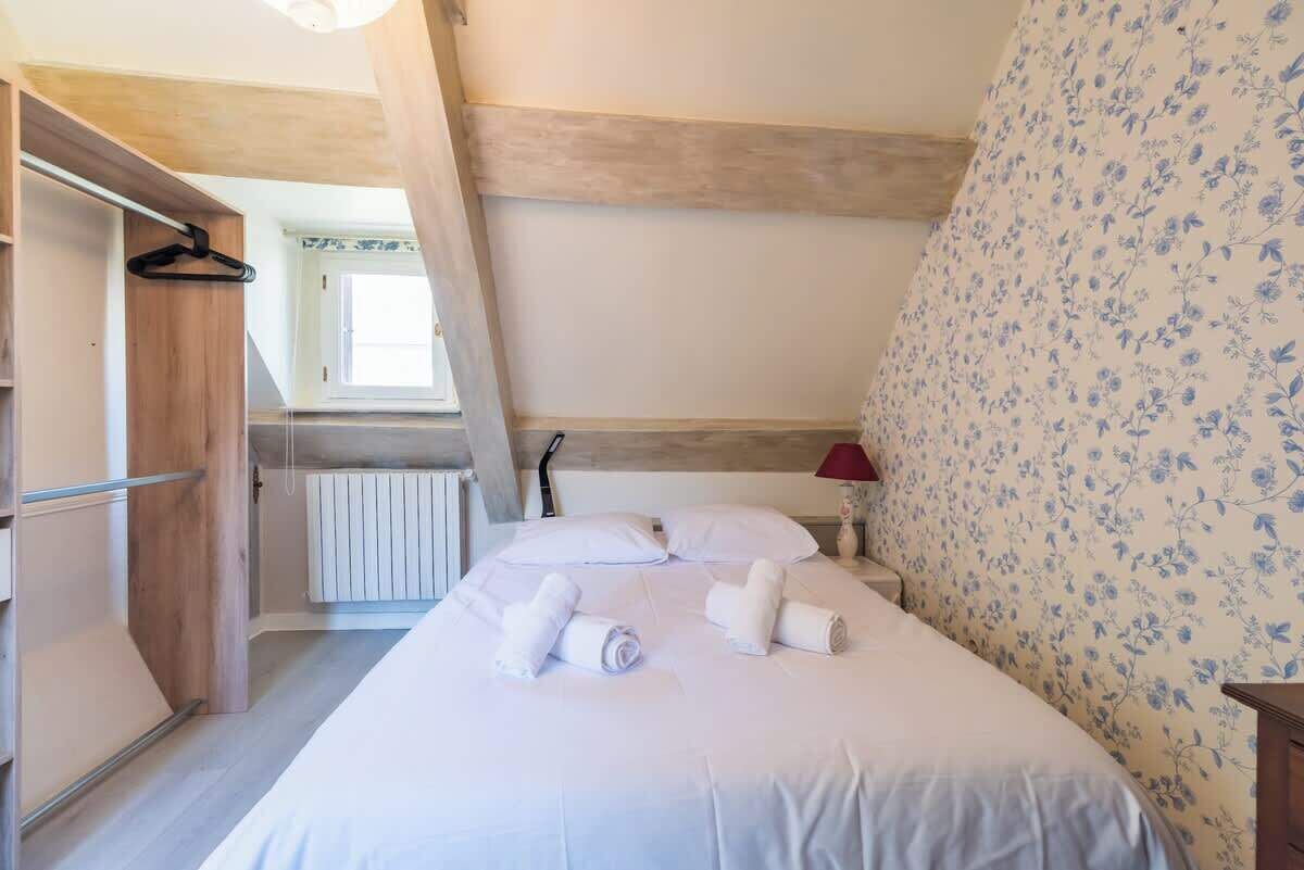 Et soveværelse med en seng, puder, en radiator, et træskab og et vindue.