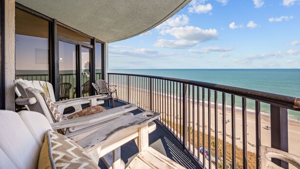 Un balcon avec vue sur la plage, une table et deux chaises.
