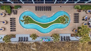 Vue aérienne d’une piscine avec des chaises longues, des palmiers et un espace paysager aménagé.