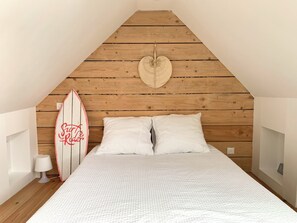 A bedroom with a wooden sloped ceiling, a surfboard, two white pillows, and a white bedspread. - A charming little fisherman's cottage 150 meters from the ocean and in the center of Loctudy (Loctudy)