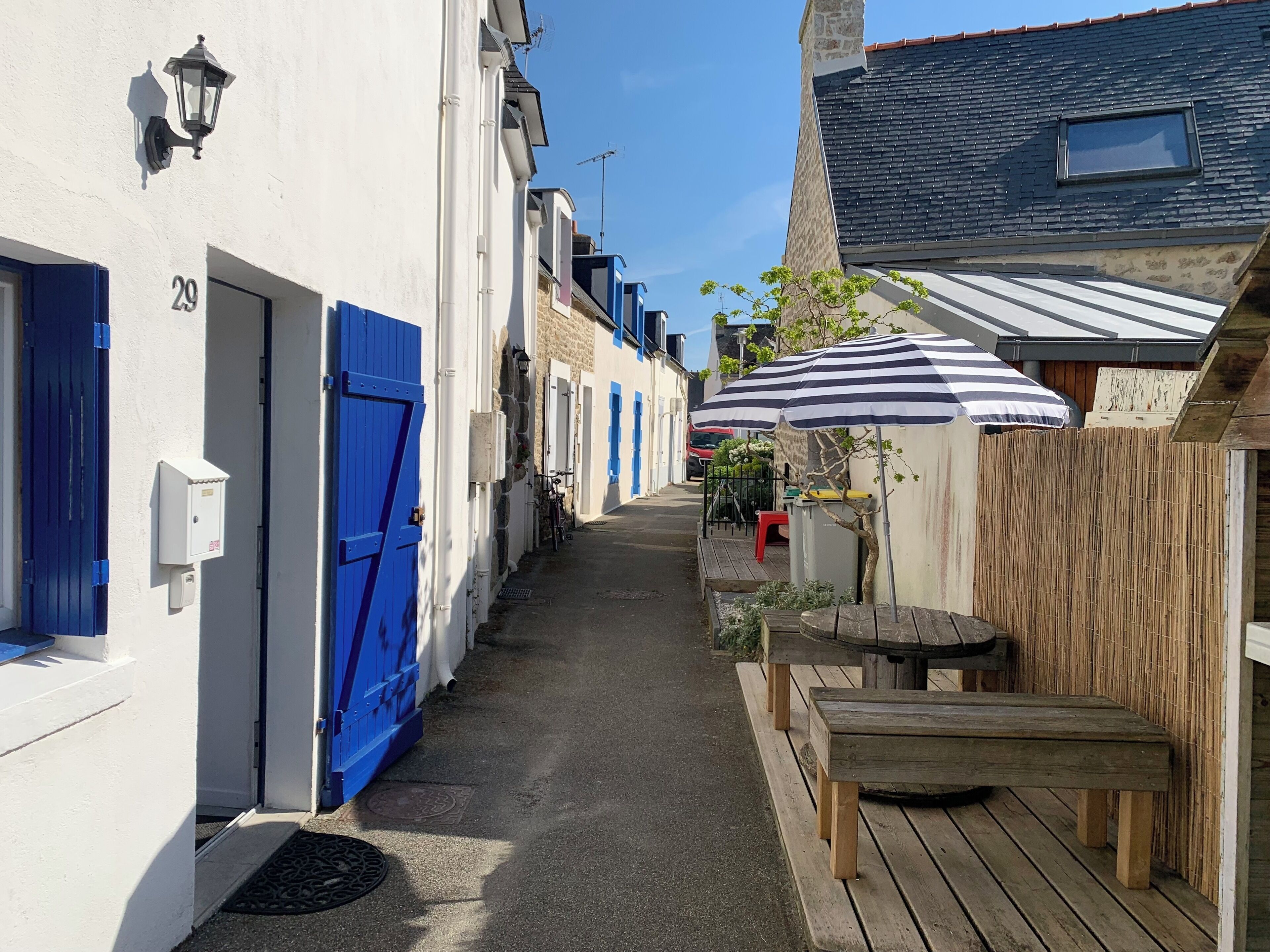 A narrow street with white buildings, blue doors, and a wooden bench.