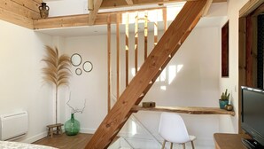 Ein Zimmer mit einer Holztreppe, einem weißen Stuhl, einem Fernseher und einem Bett mit floralem Überwurf.