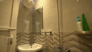 Baño con lavamanos, espejo, ducha y artículos de aseo.