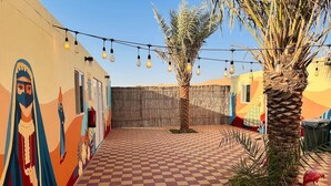 Un patio con suelo a cuadros, palmeras y luces colgantes.