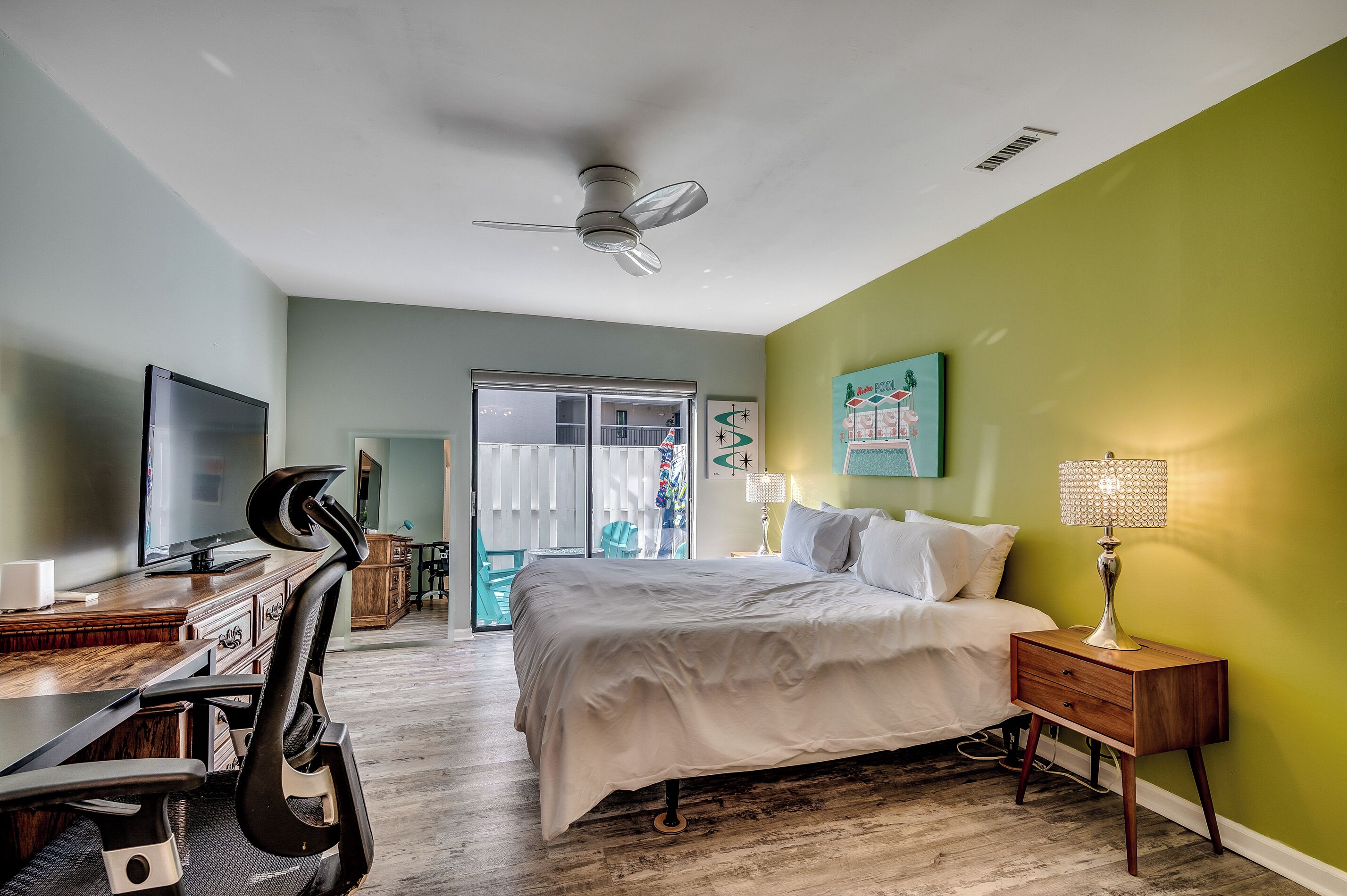 A bedroom with a bed, desk, chair, TV, and a ceiling fan.