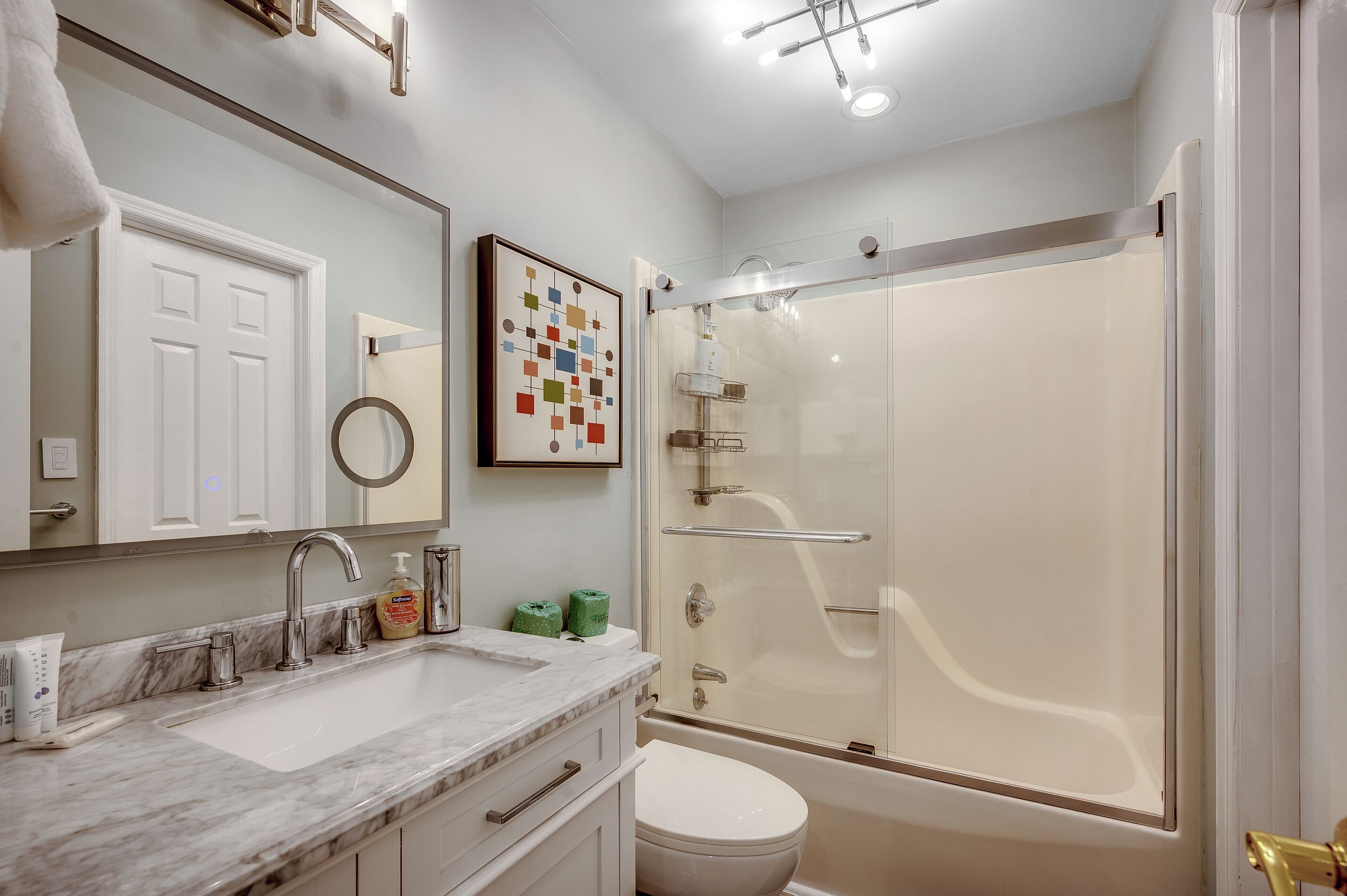 A bathroom with a marble sink, a toilet, a glass-enclosed shower, and a framed artwork on the wall.