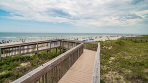 A wooden boardwalk leading to a beach with people and umbrellas.