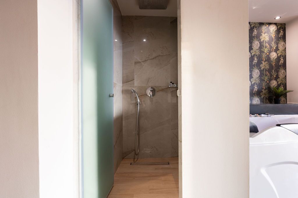 A modern bathroom with a shower, marble walls, and a wooden floor.