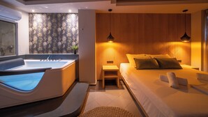 A modern bedroom with a large bed, a small bedside table, a built-in bathtub, and a wooden wall panel. - HOM54 Luxury Suites (Heraklion)