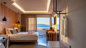A modern hotel room with a bed, desk, and large window offering a view of the mountains. - HOM54 Luxury Suites (Heraklion)