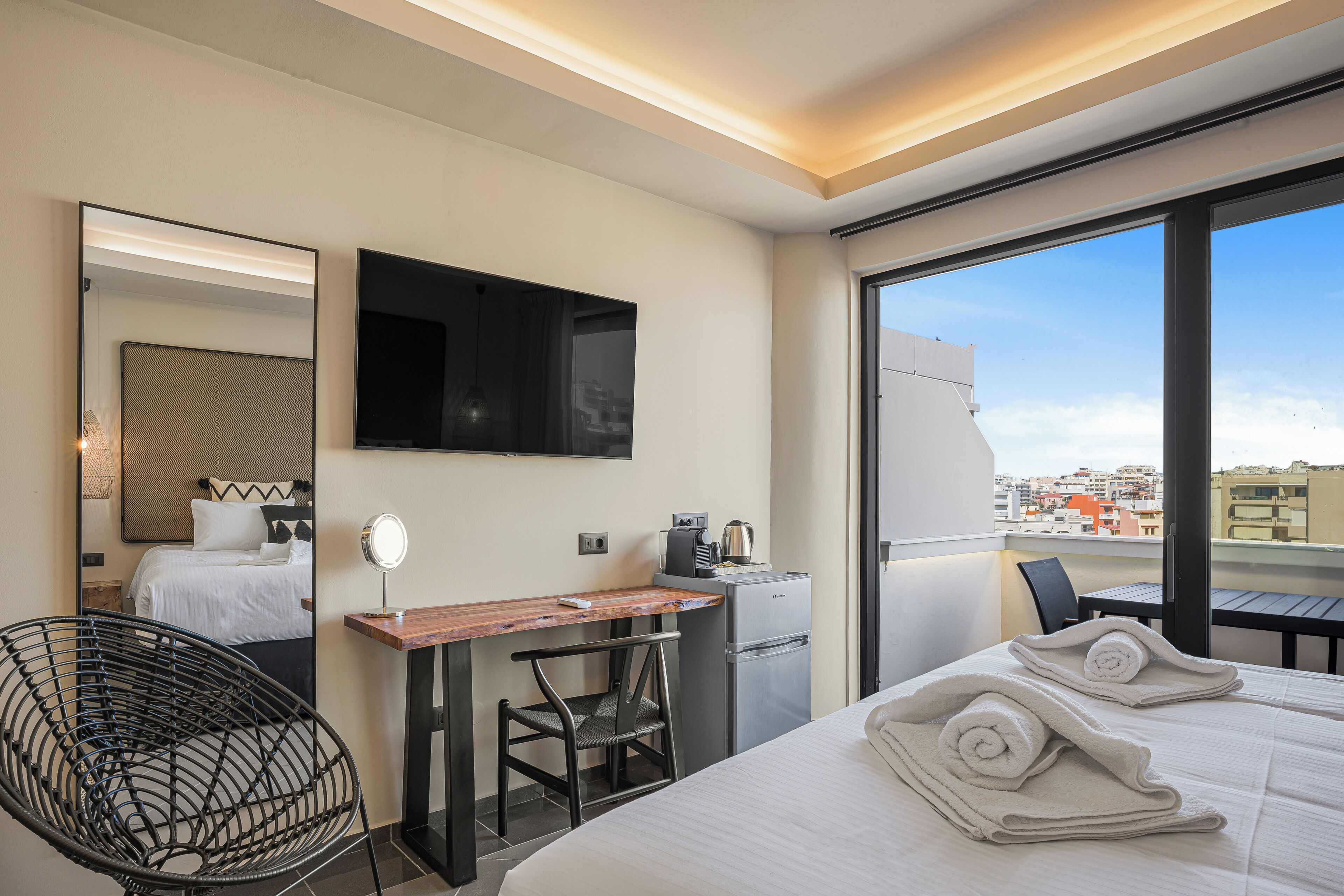 Ein Hotelzimmer mit Bett, Schreibtisch mit Computer, Stuhl, kleinem Kühlschrank, Spiegel und Fernseher an der Wand.