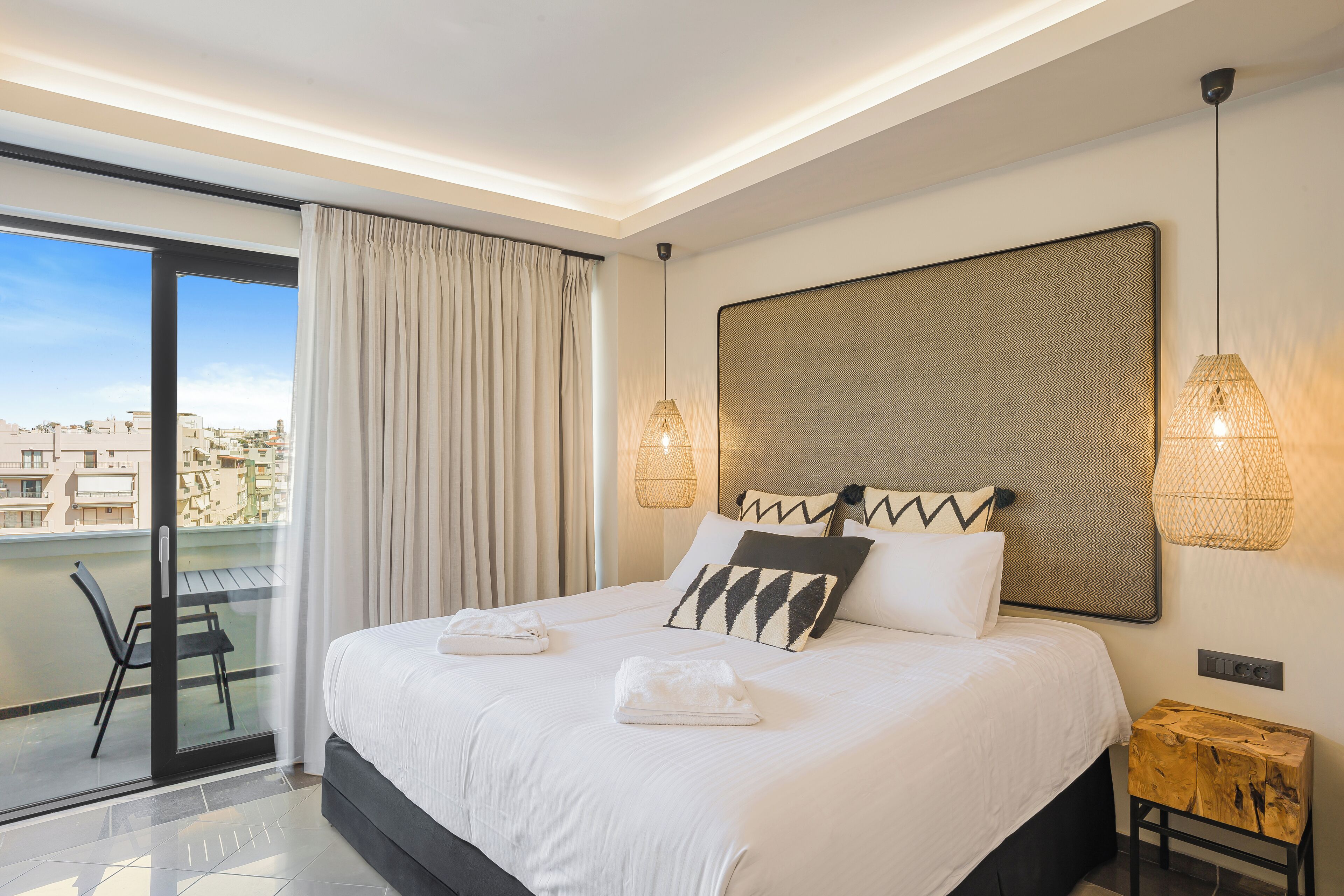 Una habitación de hotel moderna con una cama grande, un balcón con vistas y un cabecero elegante.