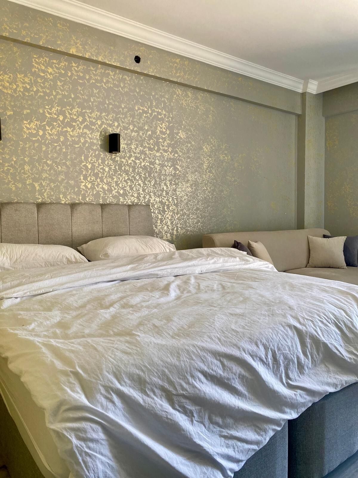 A large bed with white linens, a grey headboard, and a wall with a gold leaf pattern.