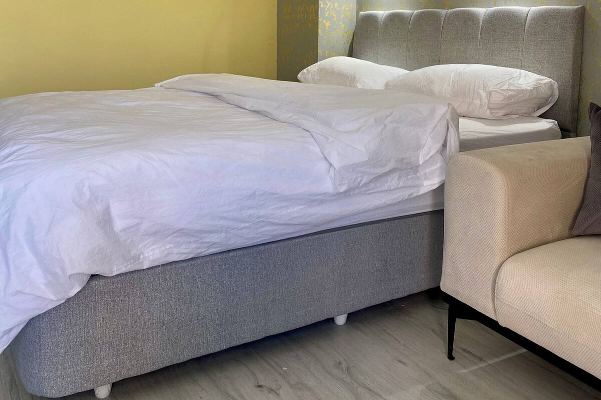 Un dormitorio con una cama doble, un sofá tapizado en gris y un sillón pequeño.