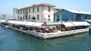 A waterfront restaurant with outdoor seating and a modern glass structure.