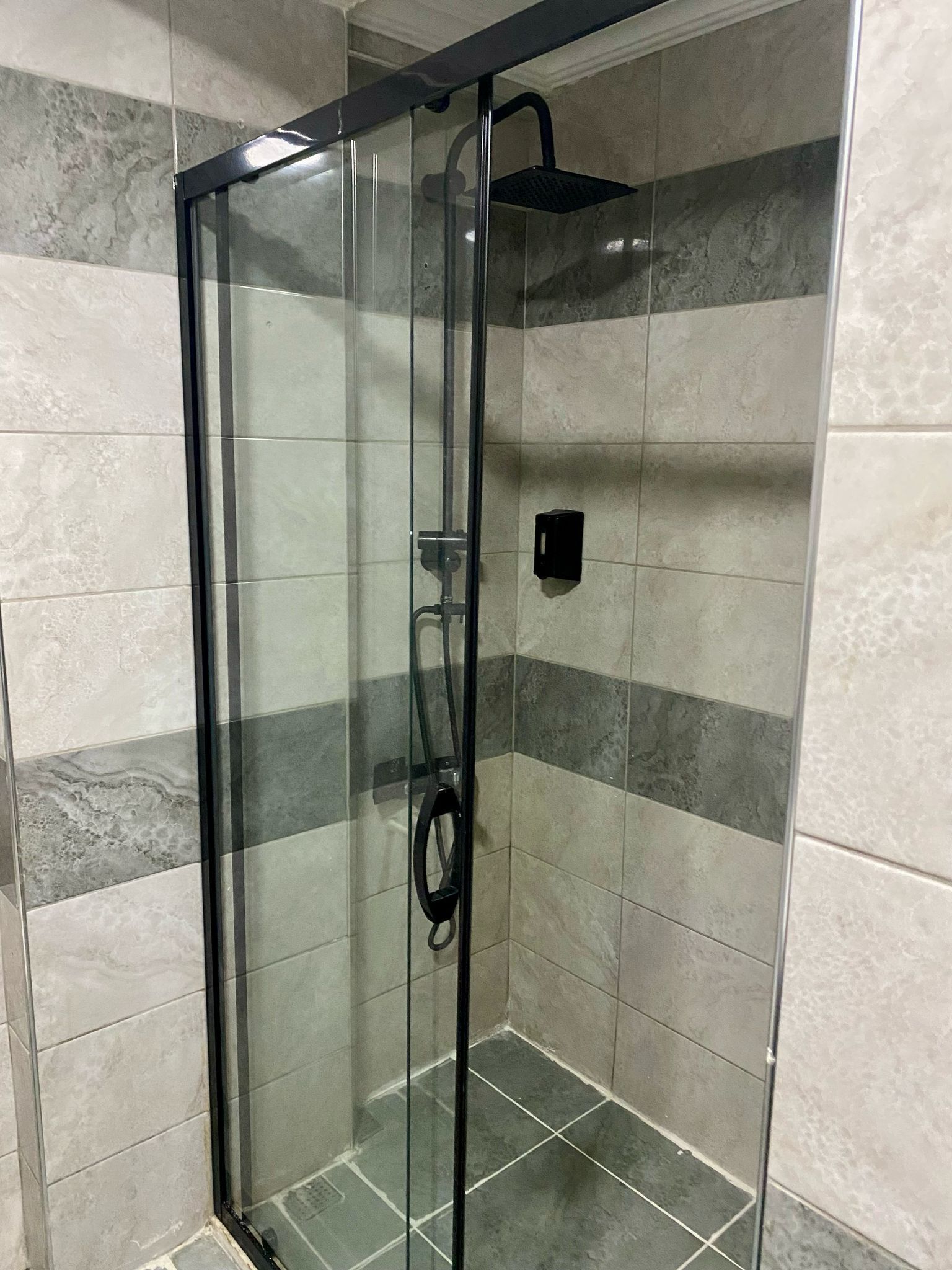 Cabina de ducha con paredes de vidrio, cabezal de ducha de mano y llave de pared.