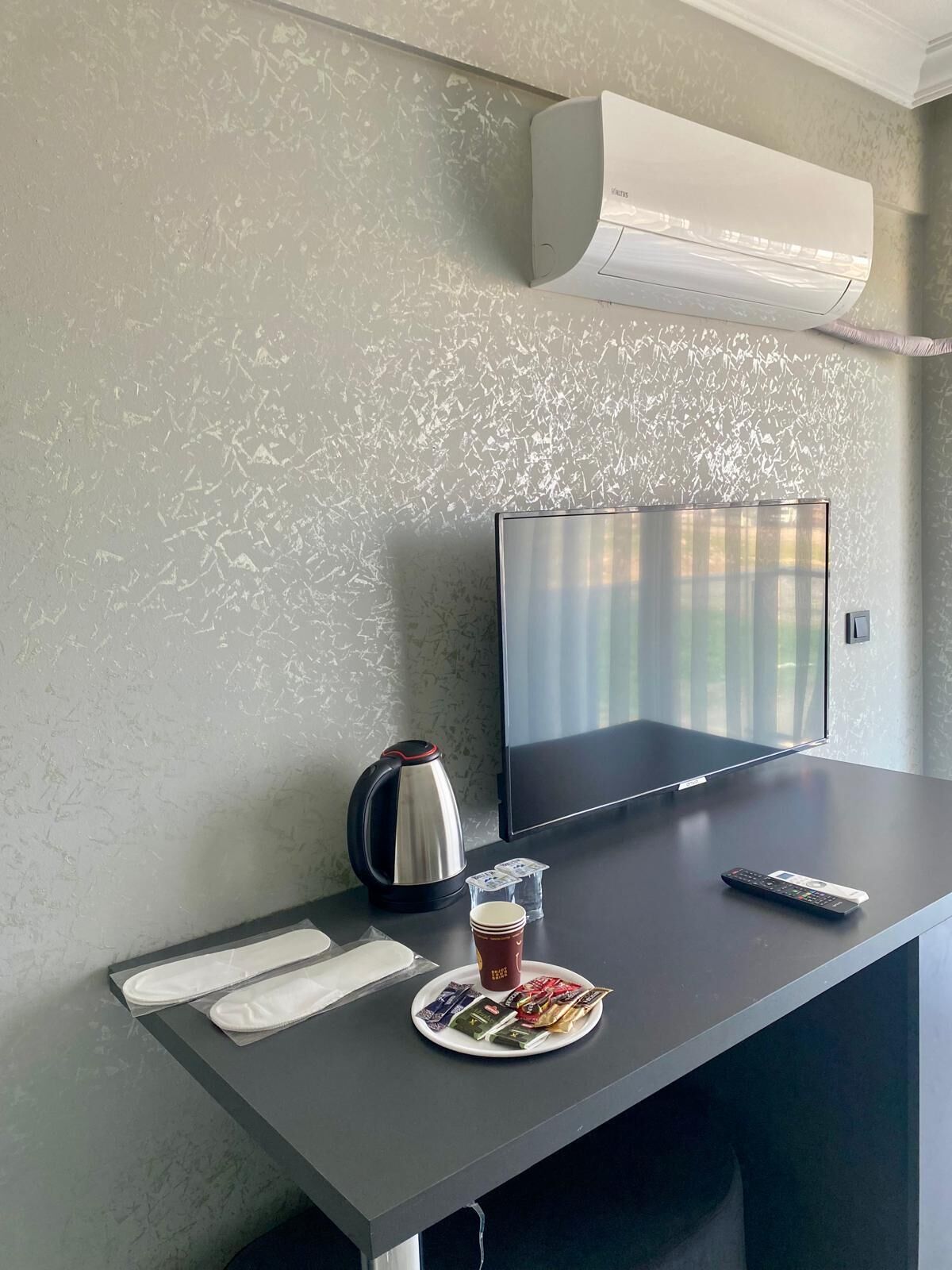 Una habitación de hotel moderna con una televisión de pantalla plana, un hervidor, un control remoto y un plato con aperitivos y una taza sobre el escritorio.