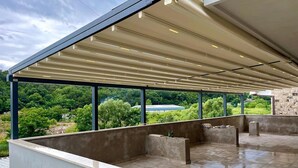 A covered outdoor terrace with a view of greenery and a distant body of water.